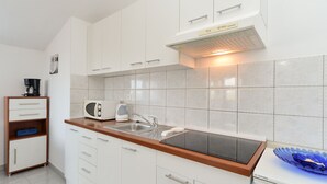 Eine kompakte Küche mit weißen Schränken, einer schwarzen Arbeitsplatte, einer Mikrowelle, einem Wasserkocher und einem kleinen Kühlschrank.