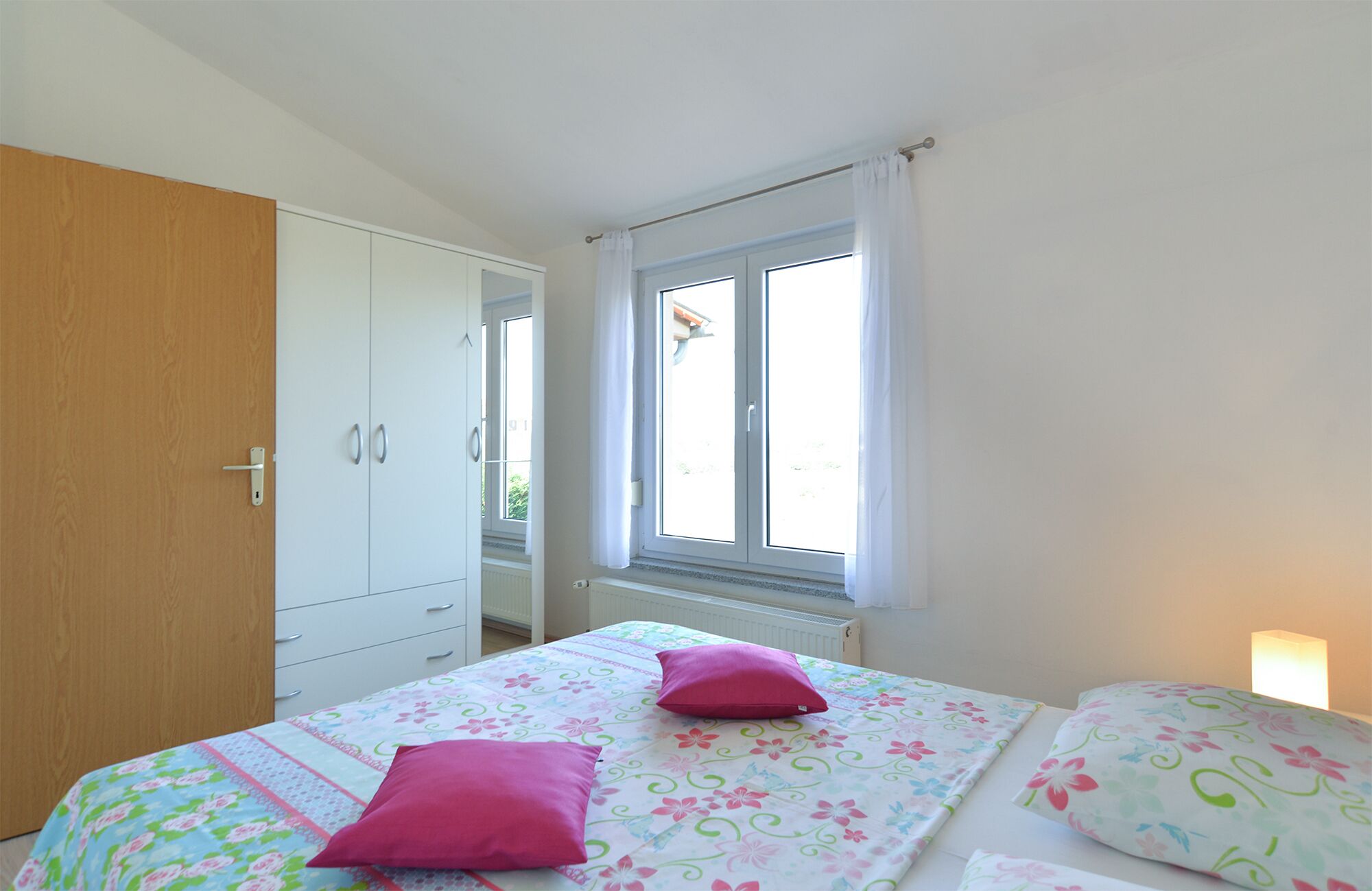 A bedroom with a bed, two pillows, a window, and a wardrobe.