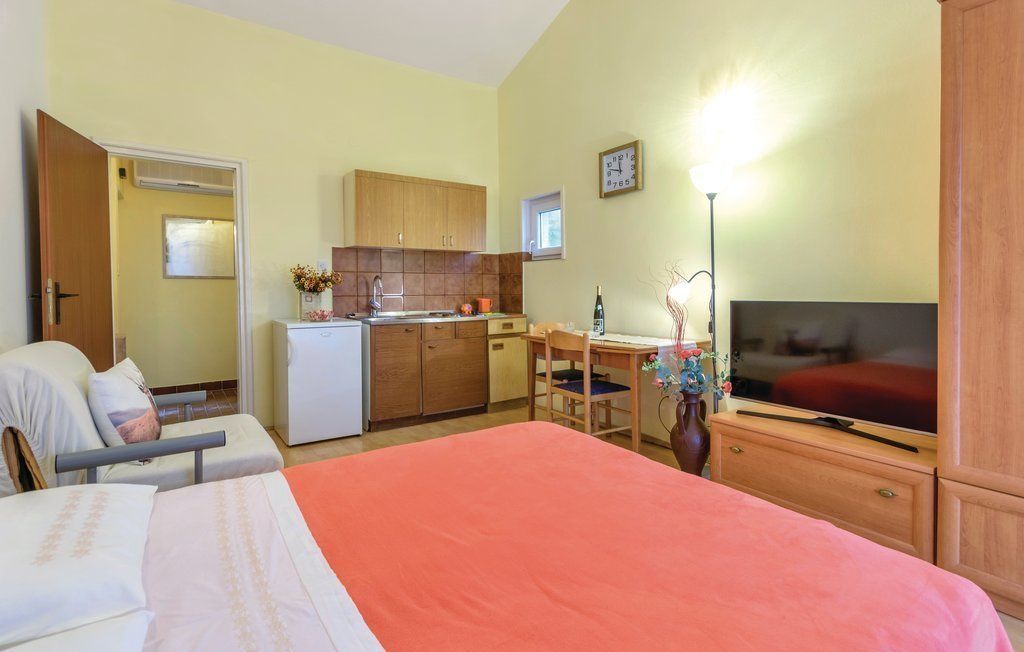 A hotel room with a bed, a desk, a television, a kitchenette, and a bathroom.