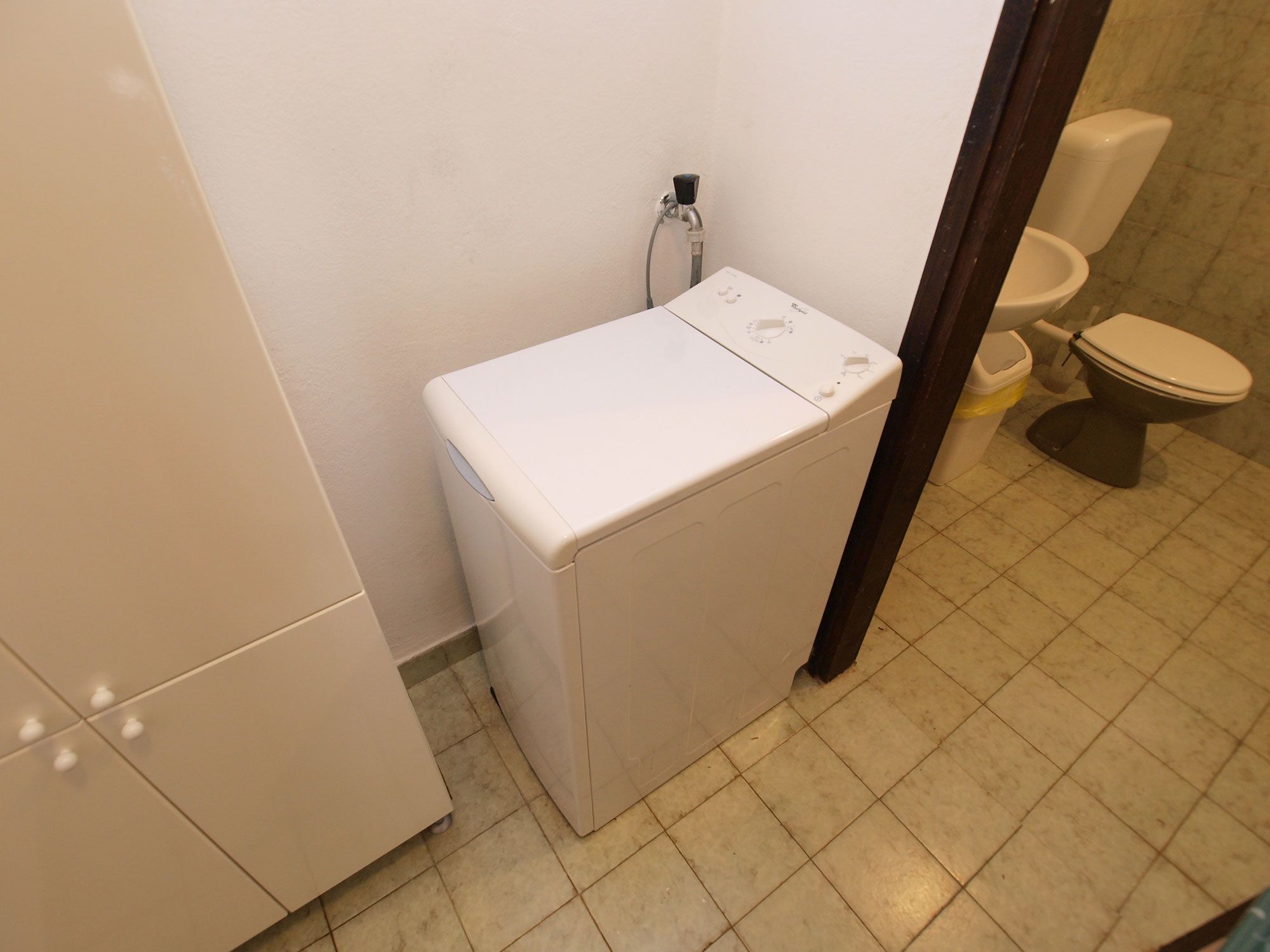 A compact bathroom with a white washing machine, a toilet, and a sink.