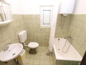 Et lille badeværelse med toilet, håndvask og badekar.