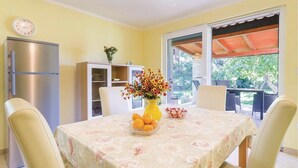 A dining area with a table set for four, a yellow vase with flowers, and a bowl of oranges.