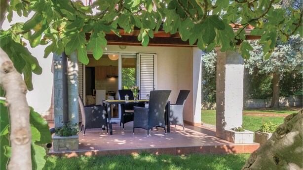 An outdoor patio with a table and chairs, a covered area with a sliding door, and a view of a building in the background.