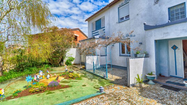 A white building with a tiled roof, a garden with colorful flowers and statues, and a blue fence. - Apartment 725 (Fazana)