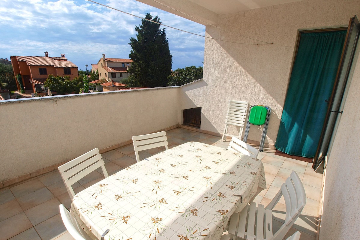 Uma varanda com mesa e cadeiras, uma cortina verde e vista para prédios e árvores.