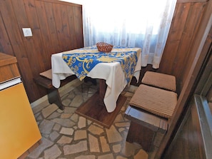 Ein Raum mit einem Tisch, der mit einer blau-goldenen Tischdecke bedeckt ist, zwei Korbstühlen, einem kleinen Korb und einem gelben Schrank.