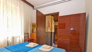 Hotellihuone, jossa on sänky, puinen vaatekaappi, tuoli ja peilillä varustettu työpöytä.