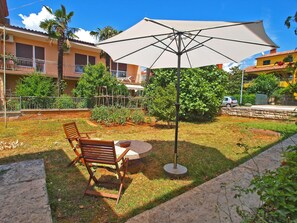 Eine Terrasse mit Tisch, zwei Holzstühlen und einem großen Sonnenschirm.