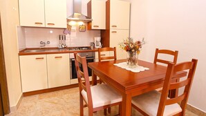 Una cocina compacta con armarios blancos, una mesa de comedor de madera con cuatro sillas, un florero y una cafetera.