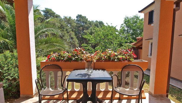 Un patio cubierto con una mesa y dos sillas, rodeado por una jardinera con flores.