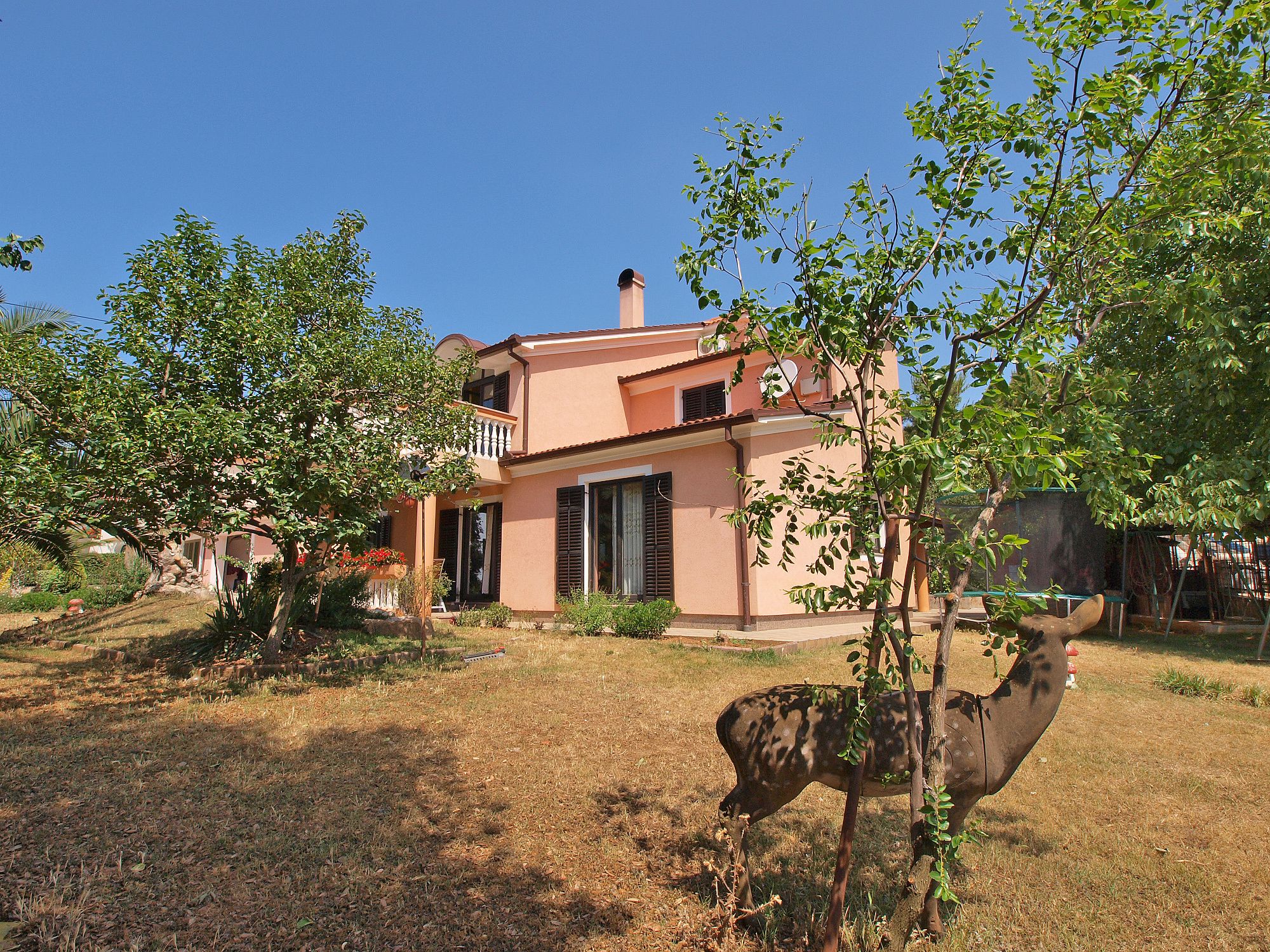 Ein zweistöckiges Haus mit Balkon, umgeben von Bäumen und einem Rasengrundstück.