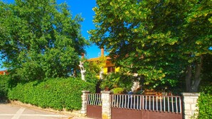 A gated entrance with a stone wall and metal gate, surrounded by lush green trees and a clear blue sky. - Apartment 731 (Pula)