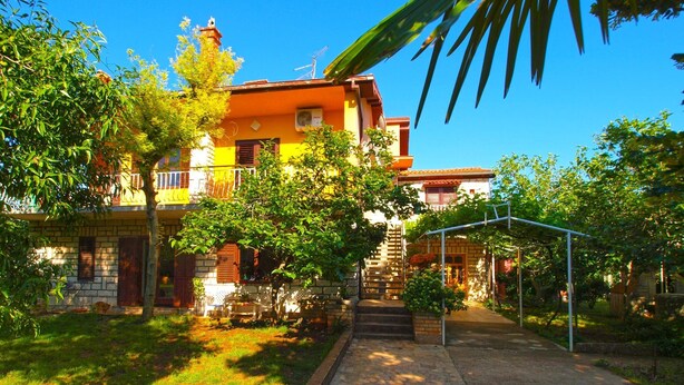 A two-story house with a stone facade, a balcony, and a garden area with a pathway leading to the entrance. - Apartment 731 (Pula)