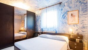 Une chambre à coucher avec un grand lit, une table de chevet avec une lampe, un miroir et une fenêtre avec des rideaux.