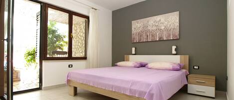 A bedroom with a bed, a nightstand, a drawer, a painting, and a window with curtains.