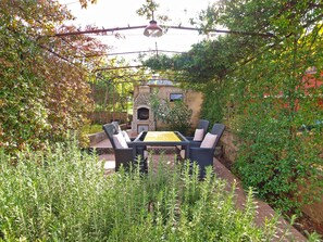 Une terrasse dotée de meubles en osier, d’un four en briques et d’une végétation luxuriante.