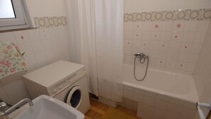 Pieni kylpyhuone, jossa on pesukone, pesuallas ja suihku.