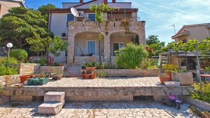 A stone building with a tiled entrance, surrounded by potted plants and a paved area. - Apartment 761 (Medulin)