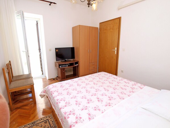 Une chambre à coucher avec un lit, un téléviseur posé sur un meuble en bois, une armoire et une chaise.