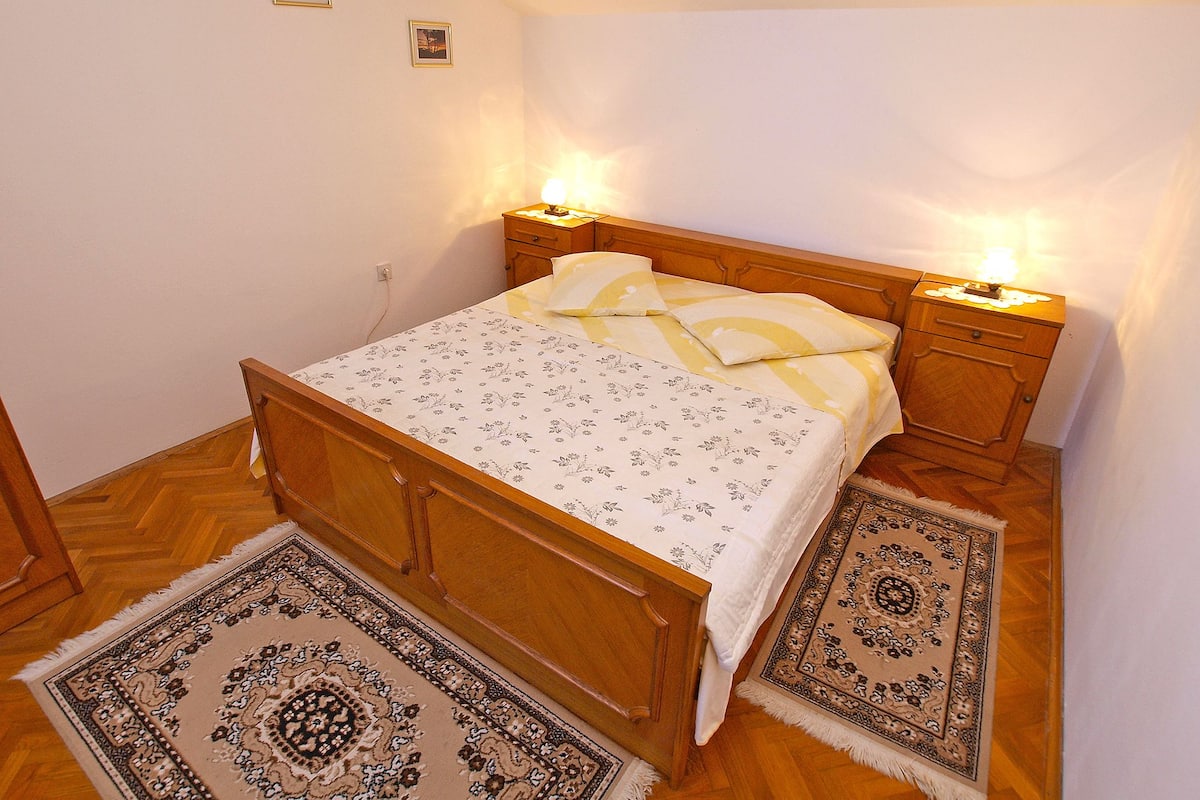A bedroom with a wooden bed, two bedside lamps, a patterned bedspread, and two rugs.