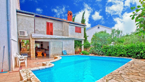 A swimming pool with stone tiles, a patio with a table and chairs, and a building with red shutters and a chimney. - Apartment 772 (Fazana)