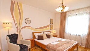 A bedroom with a bed, a chair, a nightstand, a lamp, a clock, and a window with curtains. - Apartment 772 (Fazana)