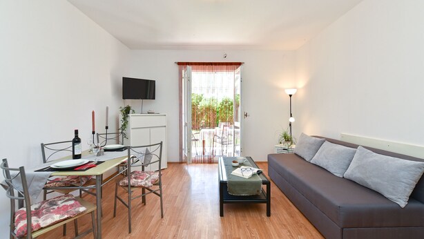 A modern living room with a sofa, dining table, chairs, and a TV mounted on the wall. - Apartment 785 (Pula)