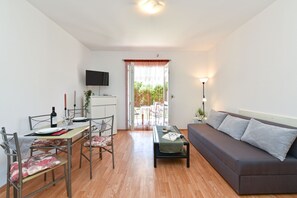 A modern living room with a sofa, dining table, chairs, and a TV mounted on the wall. - Apartment 785 (Pula)