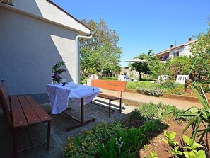 A patio with a table and benches, surrounded by a garden with various plants and a bench in the background. - Apartment 792 (Pula)