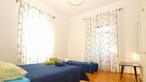 A room with two beds, wooden flooring, and curtains with a leaf pattern. - Apartment 792 (Pula)