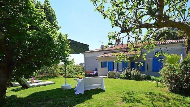 A house with a well-maintained lawn, a dining table set up outdoors, and a patio umbrella. - Apartment 792 (Pula)