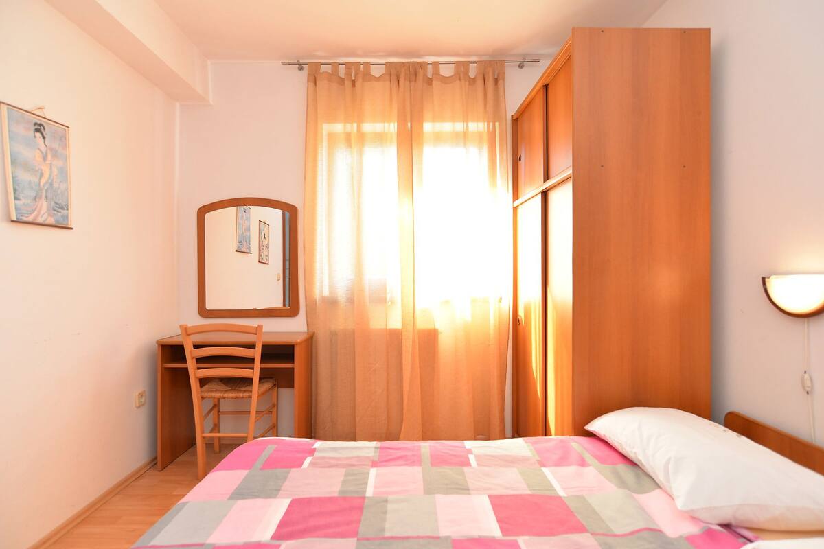 A bedroom with a bed, a chair, a desk, a mirror, and a window with curtains.