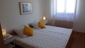 A bedroom with a bed, two bedside tables, a nightstand, a lamp, a window with sheer curtains, and a framed picture on the wall. - Apartment 802 (Porec)