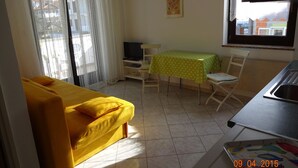 A room with a yellow sofa, a dining table with a green tablecloth, a TV, and a window with curtains. - Apartment 802 (Porec)