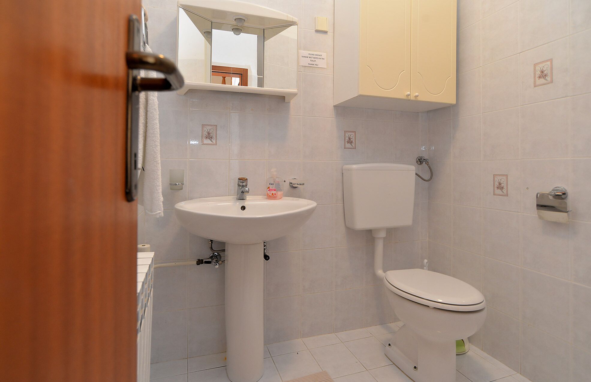 A small, clean bathroom with a white sink, toilet, and cabinet.