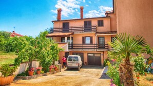 Une maison à deux étages avec un garage, entourée de plantes en pot et d’un palmier.