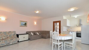 Un salon avec un canapé, une table à manger avec des chaises, un coin cuisine avec une cuisinière et un buffet.
