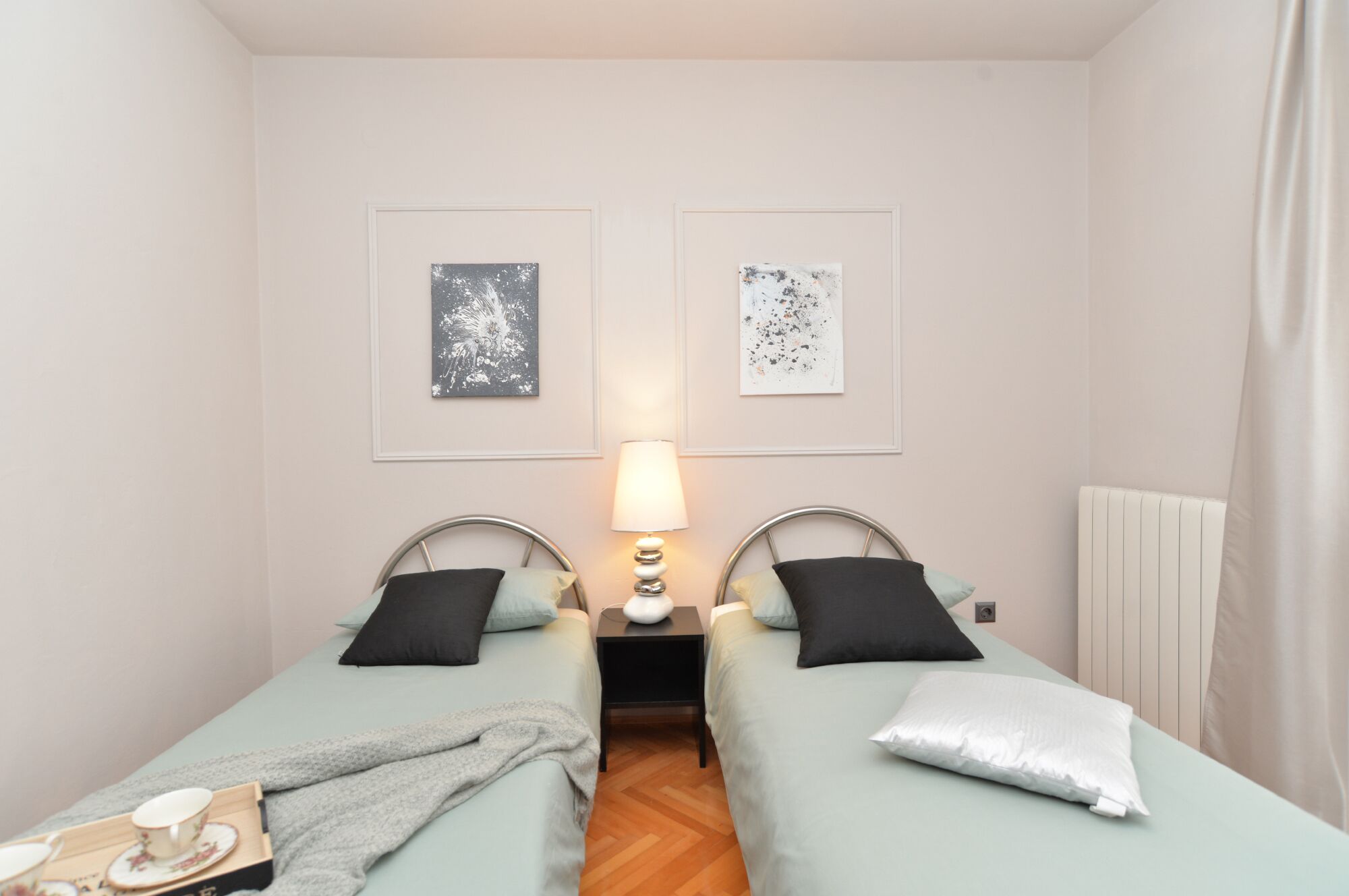 A twin room with two beds, a bedside table with a lamp, and two framed abstract artworks on the wall.