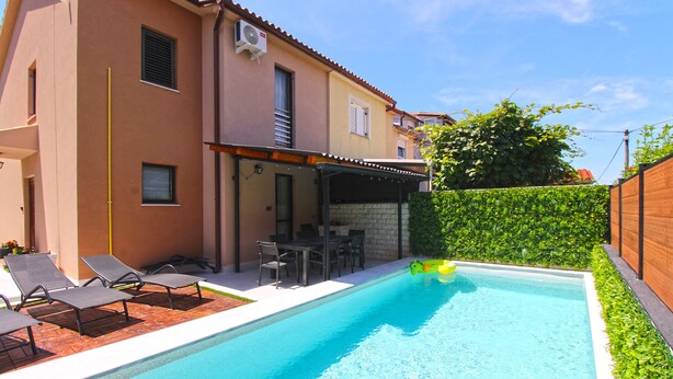 A swimming pool with lounge chairs and a table, surrounded by a wooden fence and a hedge. - Apartment 843 (Fazana)