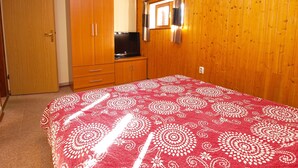 Ein Schlafzimmer mit einem Holzkleiderschrank, einem Fernseher und einem Bett mit einem gemusterten Bettüberwurf.