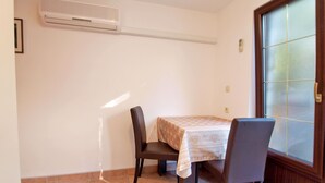 Ein kleiner Raum mit einem Tisch, zwei Stühlen, einem Fenster mit Milchglas und einer Wand-Klimaanlage.