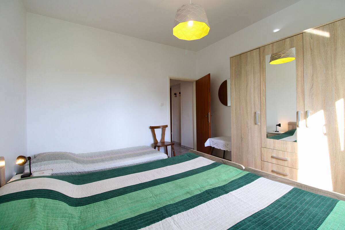 A bedroom with a bed, a wooden wardrobe, a mirror, and a hanging light fixture.