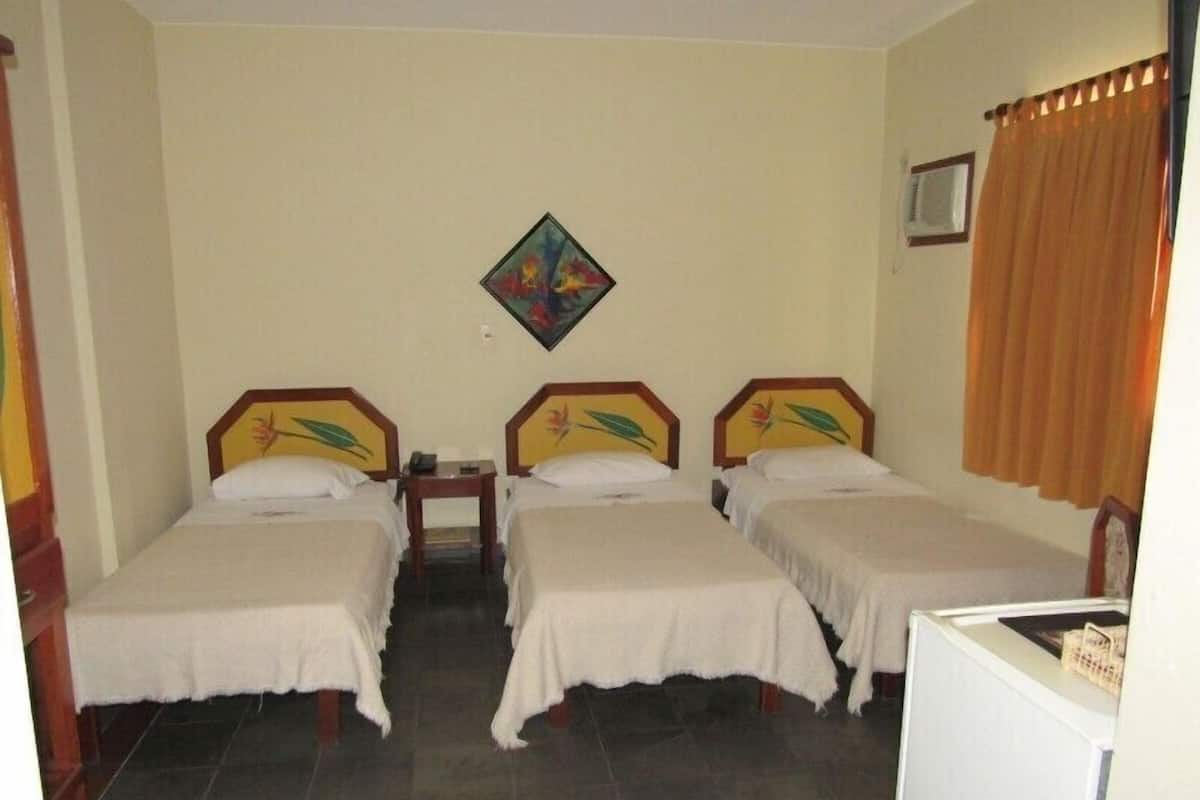 Quarto de hotel com duas camas de solteiro, uma mesinha, ar-condicionado fixado na parede e janela com cortinas.
