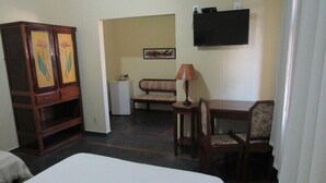 Een hotelkamer met een bed, een bureau met stoel, een bank, een kast, een lamp en een televisie aan de muur.