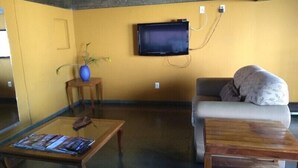 Een woonkamer met een bank, een salontafel, een aan de muur bevestigde televisie en een kleine plant op een bijzettafeltje.