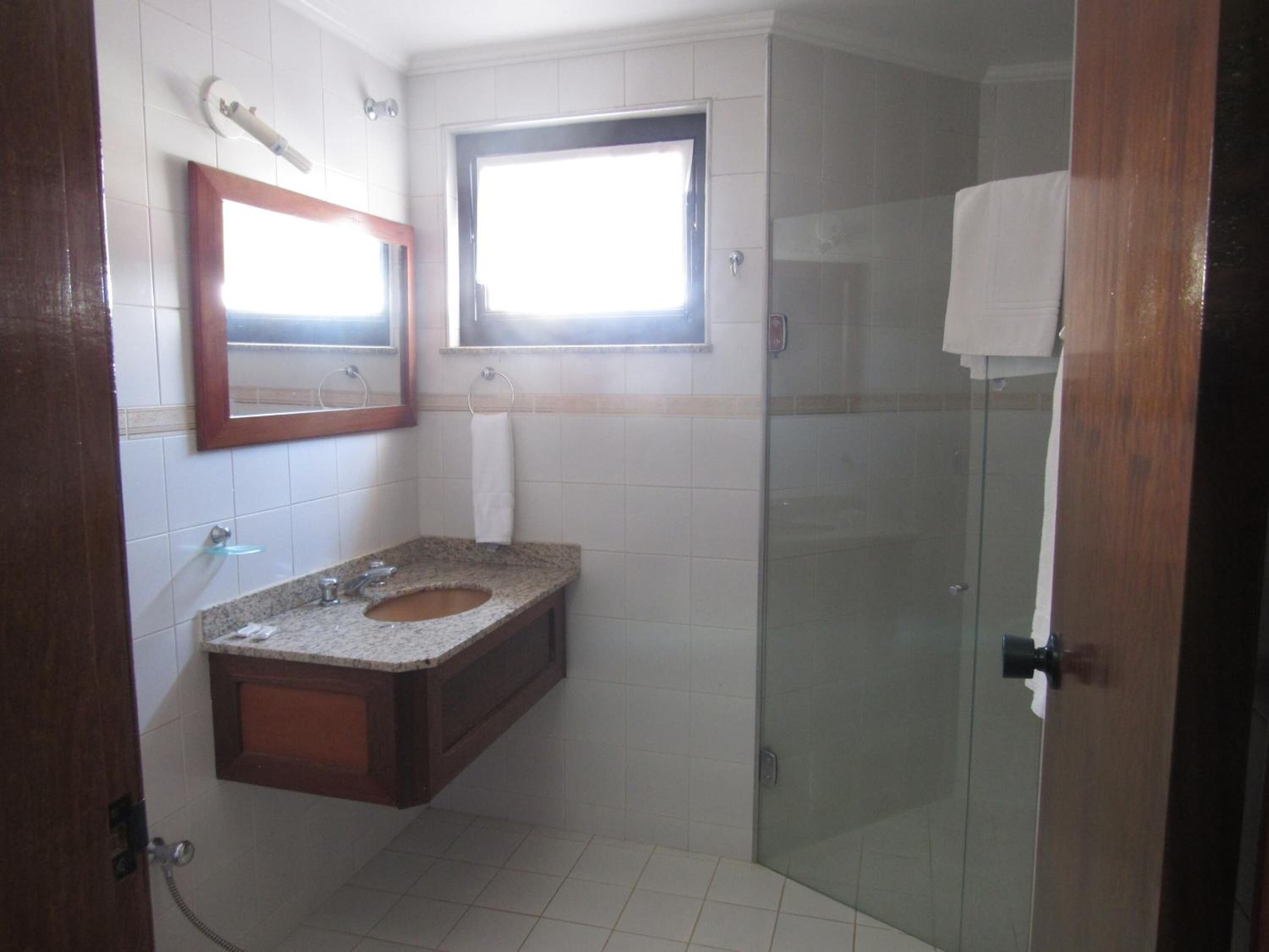 A bathroom with a granite sink, a mirror, a window, and a glass shower enclosure.