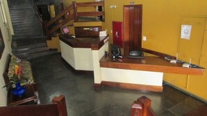 Een receptiegedeelte met een houten bureau, een rode archiefkast en een trap naar een hoger gelegen verdieping.