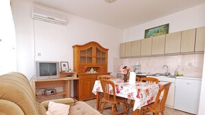 A compact living space with a sofa, a dining table with chairs, a kitchen area with cabinets, a television, and a painting on the wall. - Apartment 860 (Rovinj)