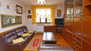 Una sala de estar con un sofá de cuero marrón, una mesa de centro de vidrio, armarios de madera y un televisor.