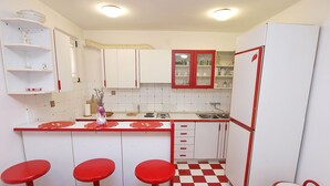Una cocina compacta con armarios blancos, detalles rojos, piso a cuadros y una barra con taburetes.